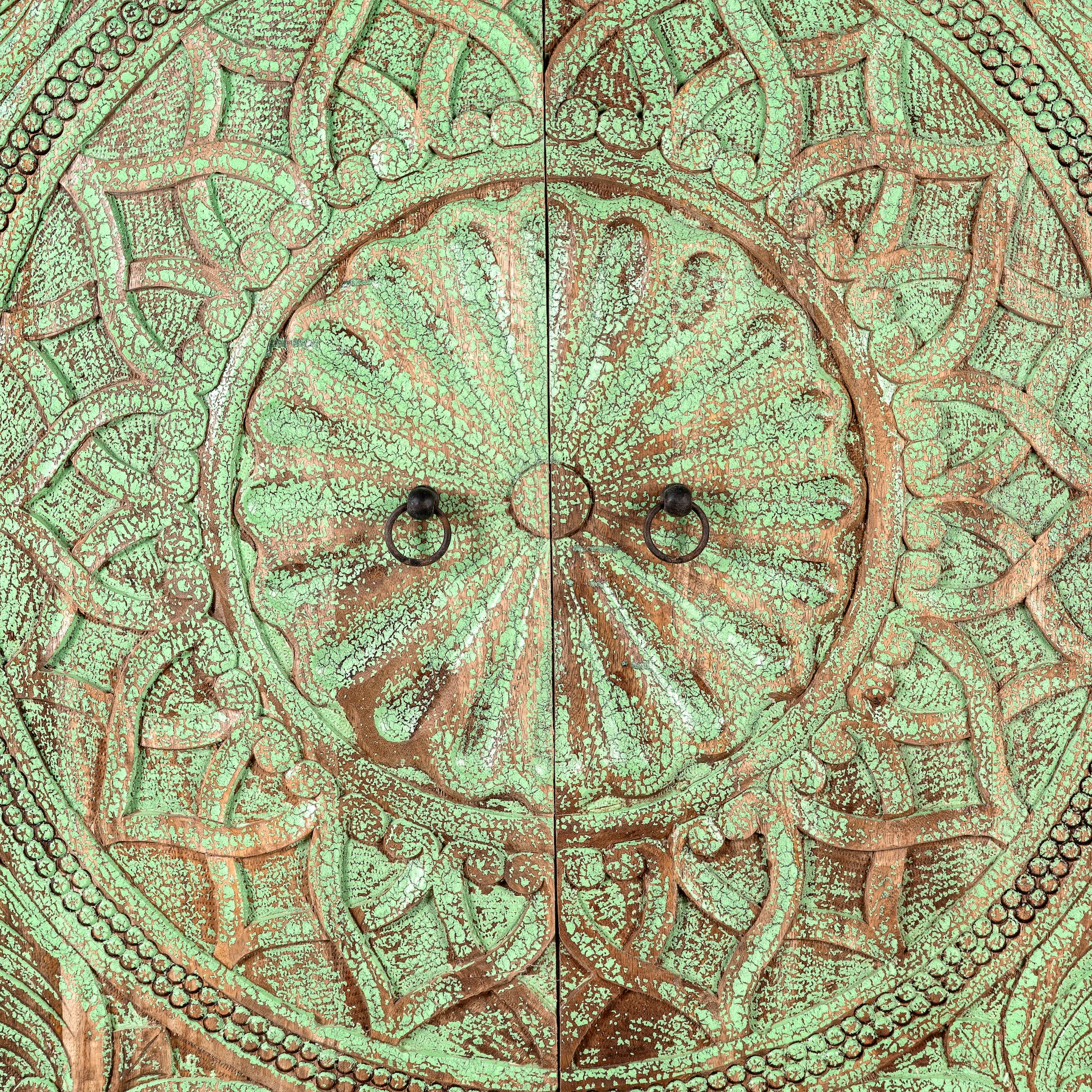 Close up image of a carved mango wood cabinet with floral hand-carving, distressed green finish, iron stand, 100 × 40 × 150 cm.