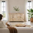 Lifestyle image with a handcrafted carved sideboard made from reclaimed wood with floral motifs and distressed finish; suitable as bedroom furniture, 180 × 40 × 100 cm.