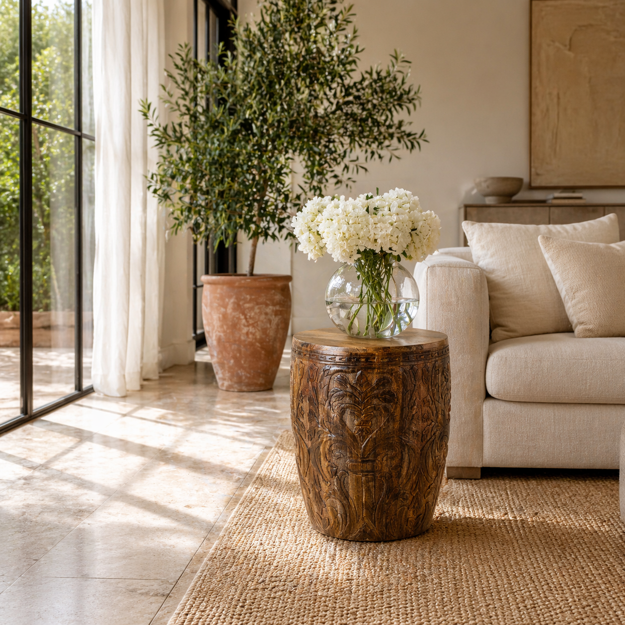 Lifestyle image of a round mango wood side table with hand carved floral design.