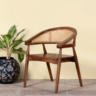 Side angle image of an acacia wood chair with curved frame and woven rattan backrest, elegant wooden armchair, 60 × 45 × 90 cm.