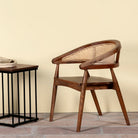 Lifestyle image of an acacia wood chair with curved frame and woven rattan backrest, elegant wooden armchair, 60 × 45 × 90 cm.