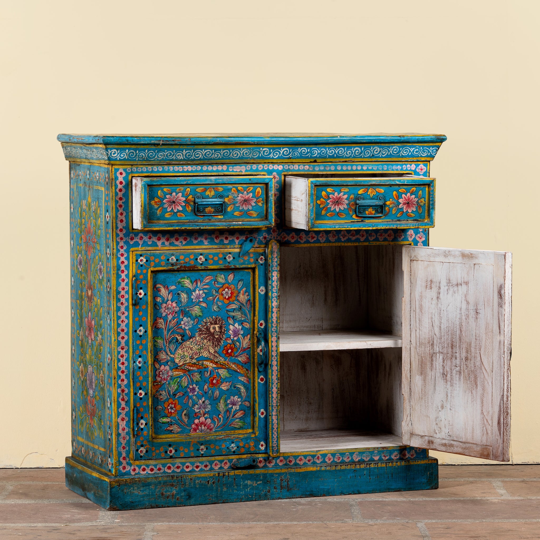 A small hand-painted wooden cabinet with turquoise blue, orange, and pink floral details, featuring two drawers and one open door showing an empty shelf, set against a plain beige background.