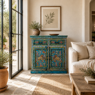 Lifestyle image of a Rajat hand-painted blue reclaimed wood cabinet with colourful floral and animal motifs, two drawers and two doors.
