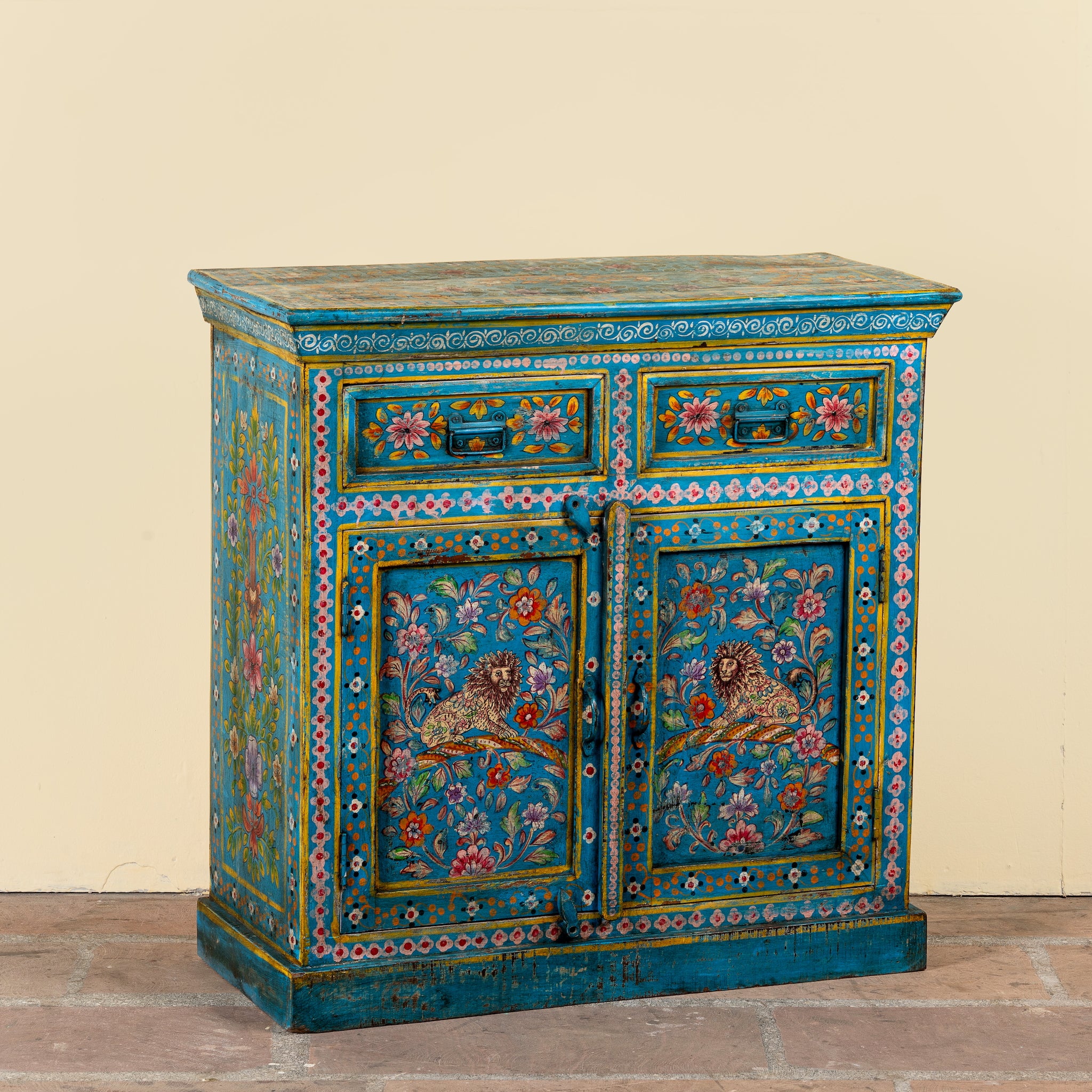 Side angle image of a Rajat hand-painted blue reclaimed wood cabinet with colourful floral and animal motifs, two drawers and two doors.