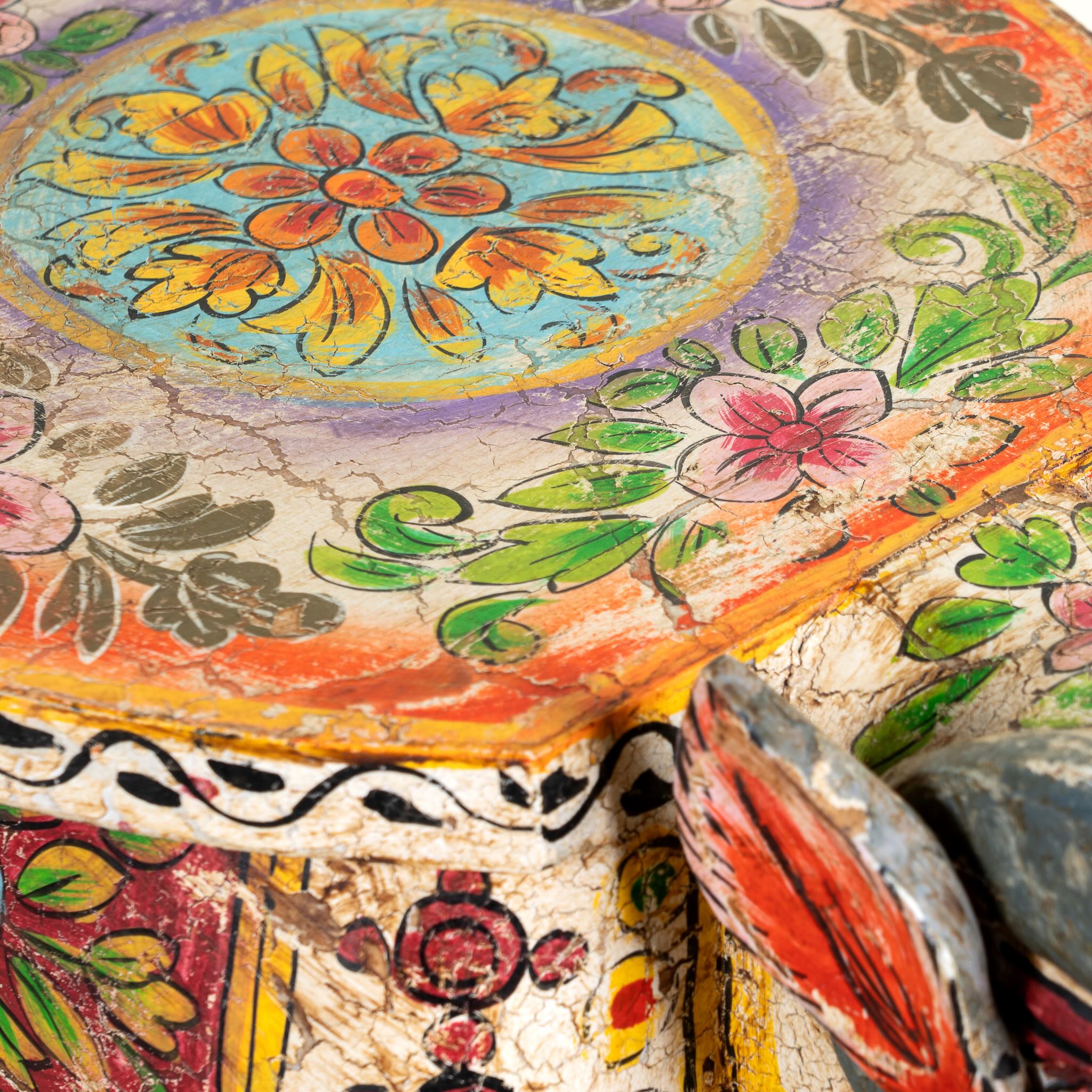 Close up image of a hand-painted wooden  side table in the shape of a ram with curved horns, featuring colourful Indian folk art patterns, ideal for vintage and India-inspired home accessories.