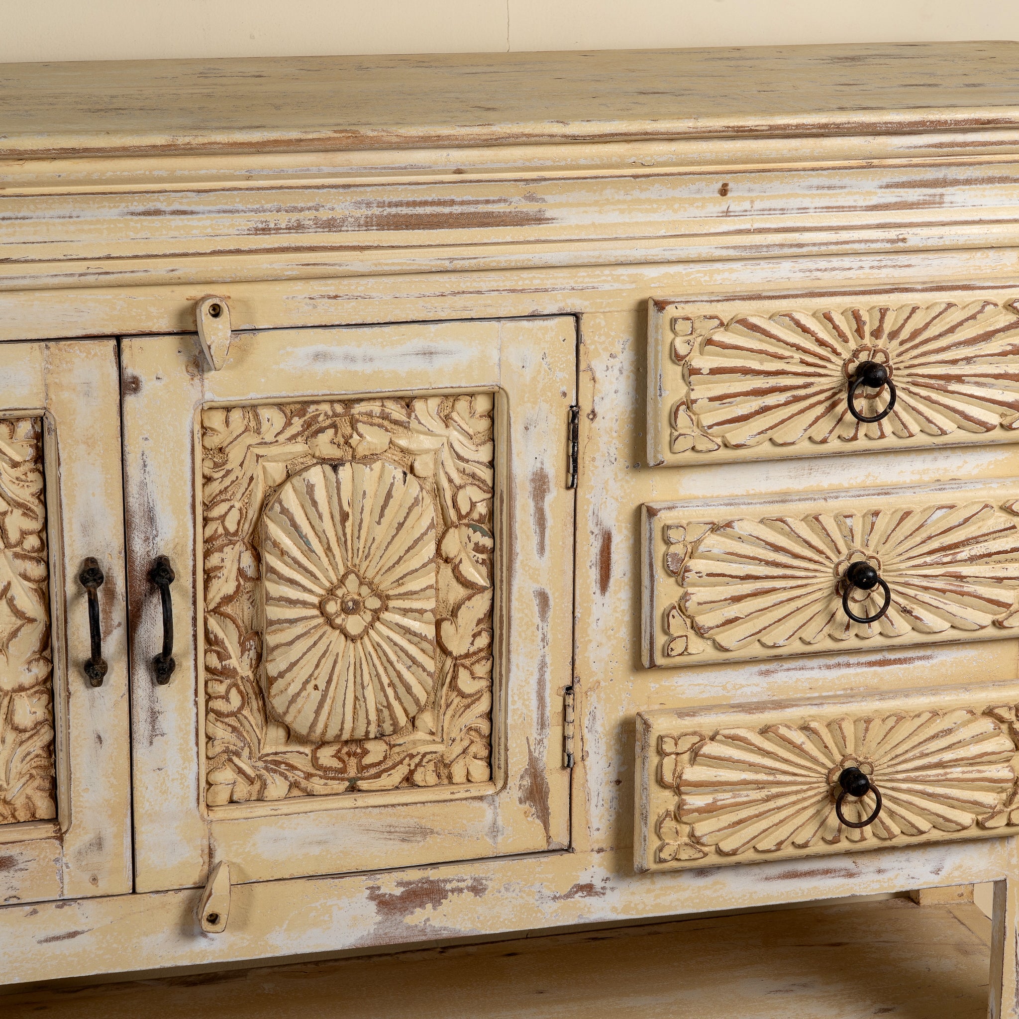 Close up image of a Ranjit reclaimed wood vintage console table with cream distressed finish, carved doors, three drawers and open lower shelf.