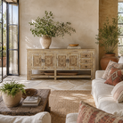 Lifestyle image of a Ranjit reclaimed wood vintage console table with cream distressed finish, carved doors, three drawers and open lower shelf.
