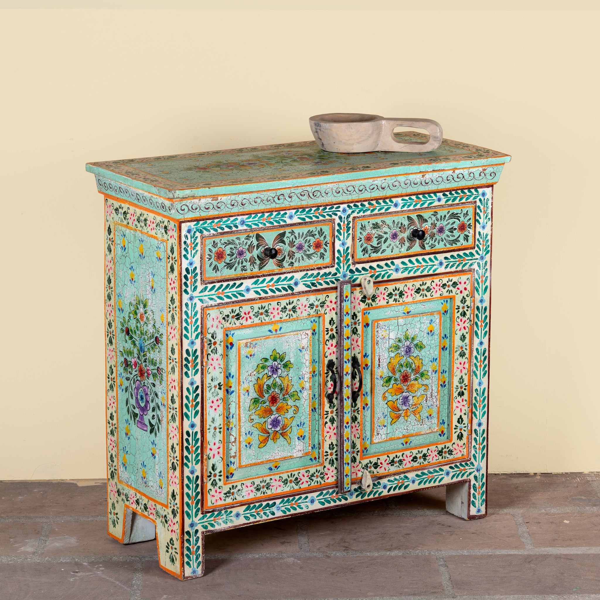 Side angle image of a hand painted green Indian cabinet made from recycled wood with floral motifs, 2 drawers and 2 compartments, 90 × 90 × 40 cm.
