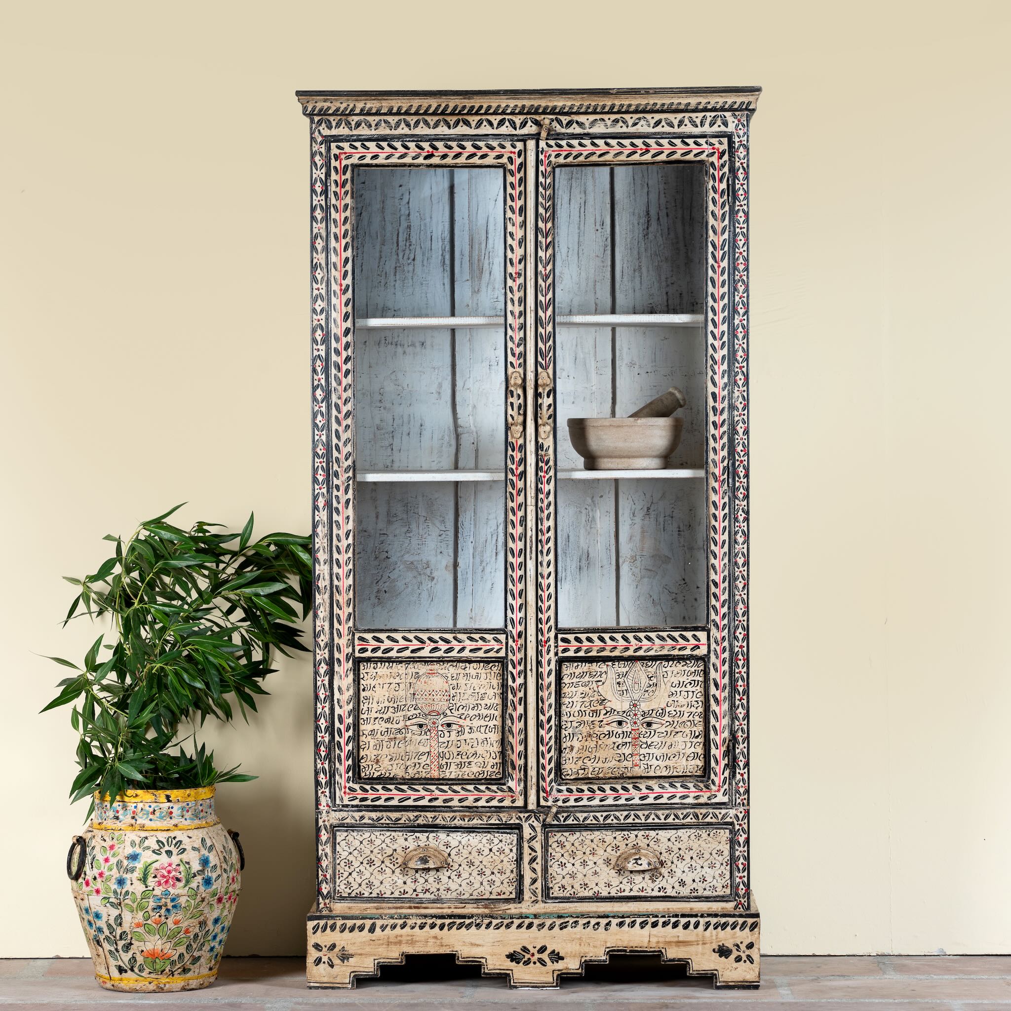 Lifestyle image of a hand-painted display cabinet Ritesh made from recycled wood with glass doors – sustainable furniture featuring Sanskrit motifs and traditional Indian craftsmanship.