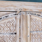 Close up picture of a cabinet made from an old teak door, featuring intricate hand-carved floral panels and a whitewashed finish- a striking piece with vintage charm and Ibiza style elegance.

