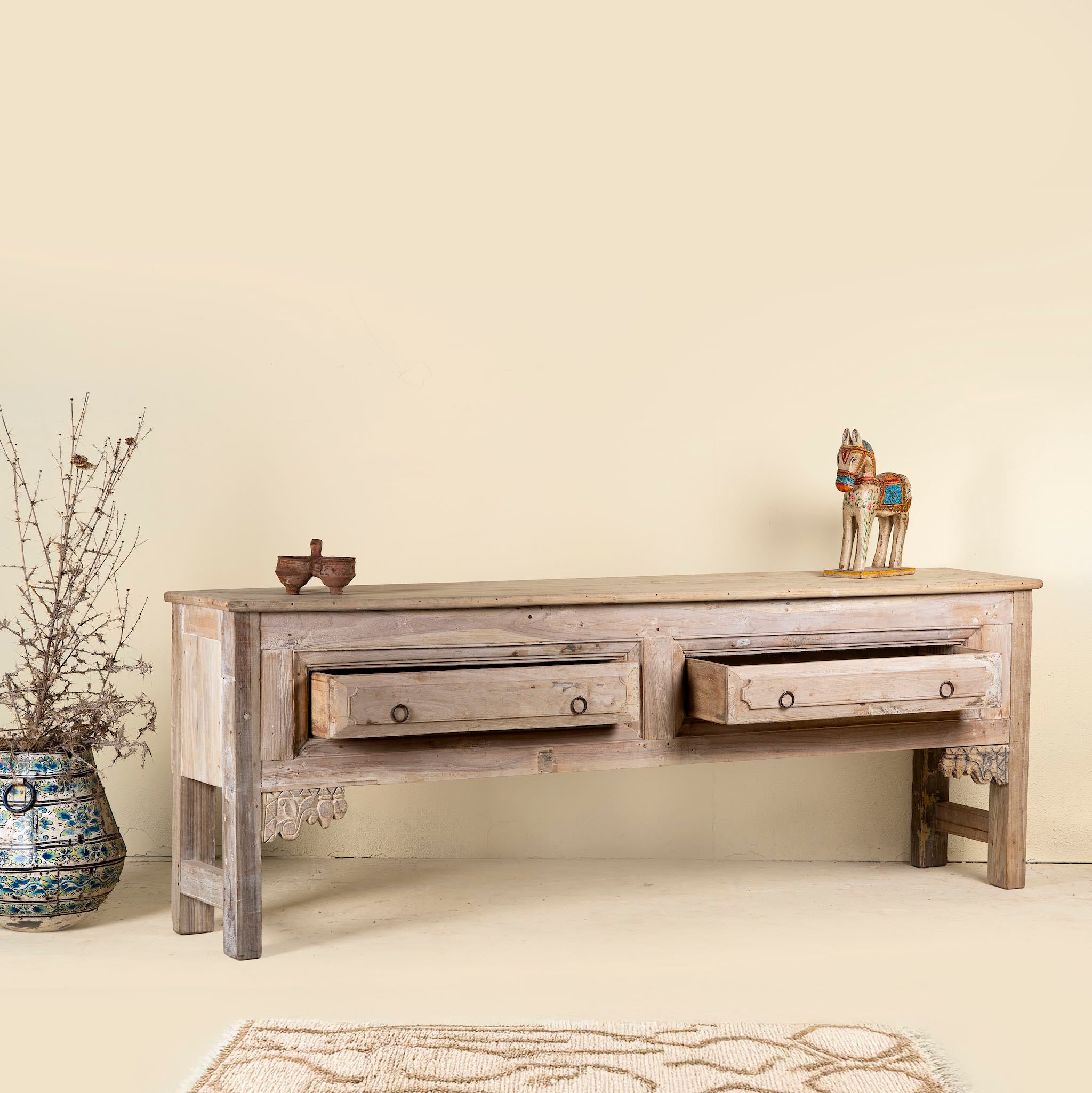 Open drawer image of a teak wood console table with two drawers, carved leg details, and sanded reclaimed finish, 223 × 45 × 83 cm.