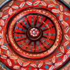 Close up image of the lid of a hand-painted round wooden box with lid, featuring traditional Indian script and decorative motifs in red, blue, and black. A unique Indian decor item used for storage or display, available in four different designs.