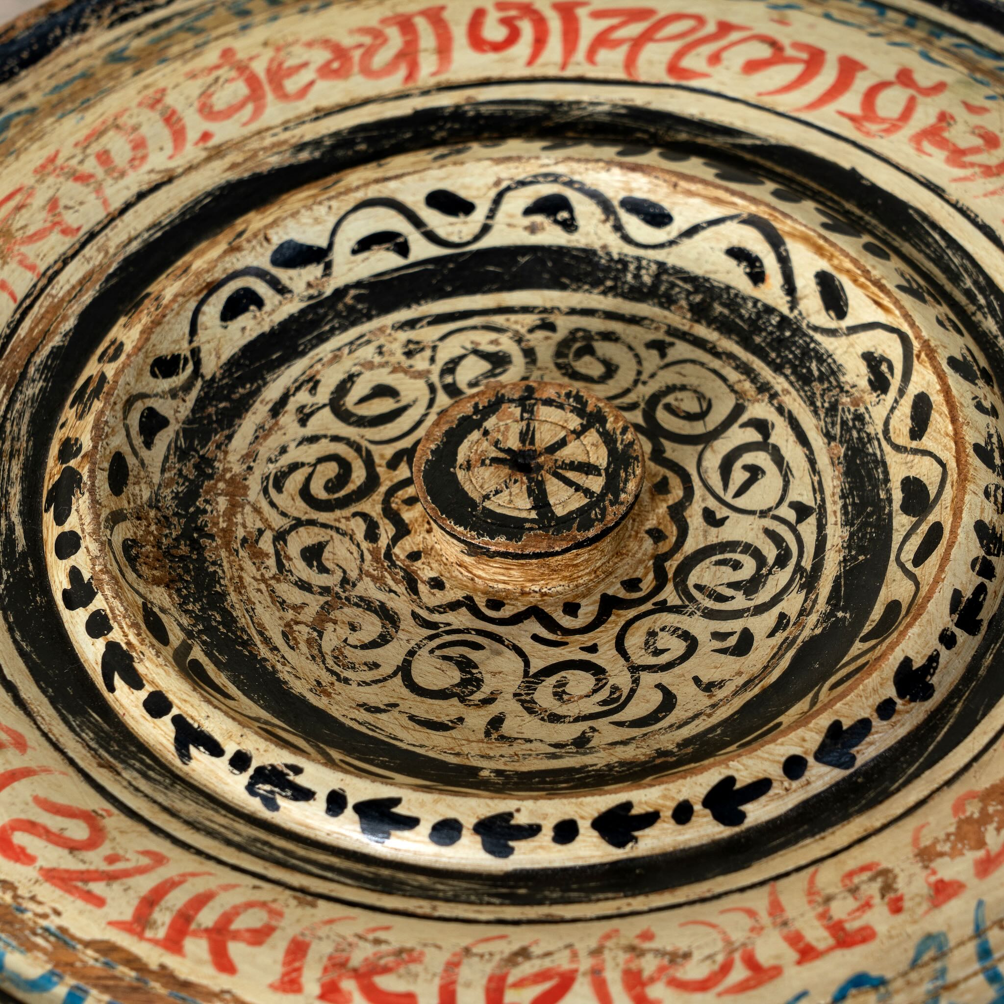 Hand-painted round wooden box with lid, featuring traditional Indian script and decorative motifs in red, blue, and black. A unique Indian decor item used for storage or display, available in four different designs.