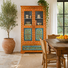 Lifestyle image of a of a hand-painted teak wood showcase with floral motifs and glass doors – sustainable furniture crafted from recycled wood with traditional Indian artistry.