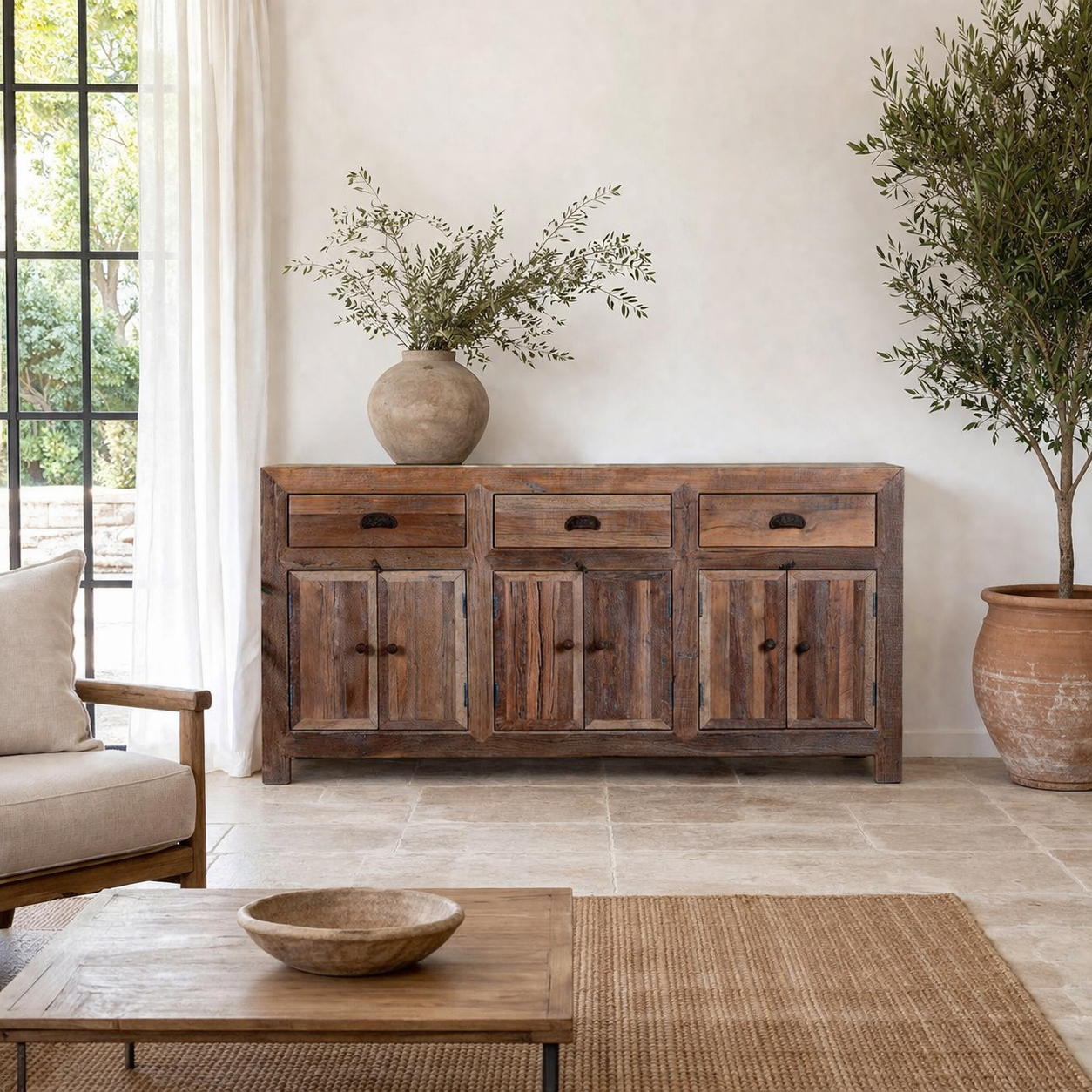 Lifestyle imagination of a reclaimed wood sideboard Amira in a rustic minimalist design, featuring three drawers and six doors with iron handles. A sustainable piece of living room furniture with natural textures and timeless appeal.