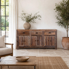 Lifestyle imagination of a reclaimed wood sideboard Amira in a rustic minimalist design, featuring three drawers and six doors with iron handles. A sustainable piece of living room furniture with natural textures and timeless appeal.