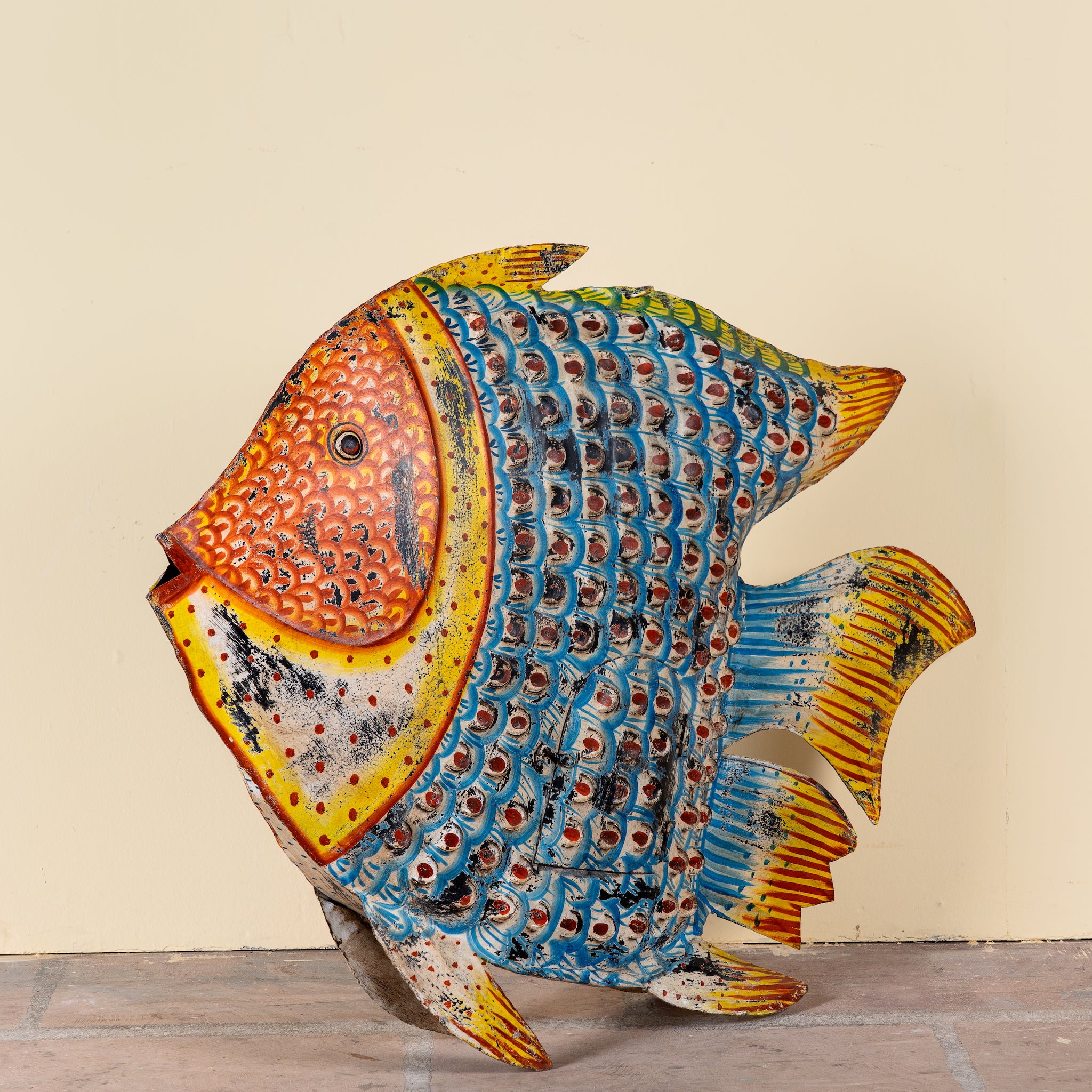 Side angle image of a Saatvik hand painted freestanding metal fish sculpture with vibrant blue, orange and yellow detailing, handcrafted decorative home accessory, 107x15x80cm.