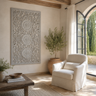 Lifestyle image of a hand-carved light grey mango wood wall panel with intricate floral openwork detailing, designed as elegant vertical wall décor with timeless artisan character.