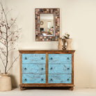 Lifestyle image of a hand-carved mango wood chest of drawers Safita with distressed blue finish and iron fittings, boho style living room furniture, 140 × 42 × 100 cm.