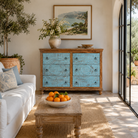 Lifestyle image of a hand-carved mango wood chest of drawers Safita with distressed blue finish and iron fittings, boho style living room furniture, 140 × 42 × 100 cm.