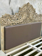 Close up of the head board of a hand-carved vintage bed Samar made from distressed mango wood, featuring an ornate high headboard with soft grey fabric upholstery. A unique blend of Indian craftsmanship and contemporary comfort in a natural, neutral palette.