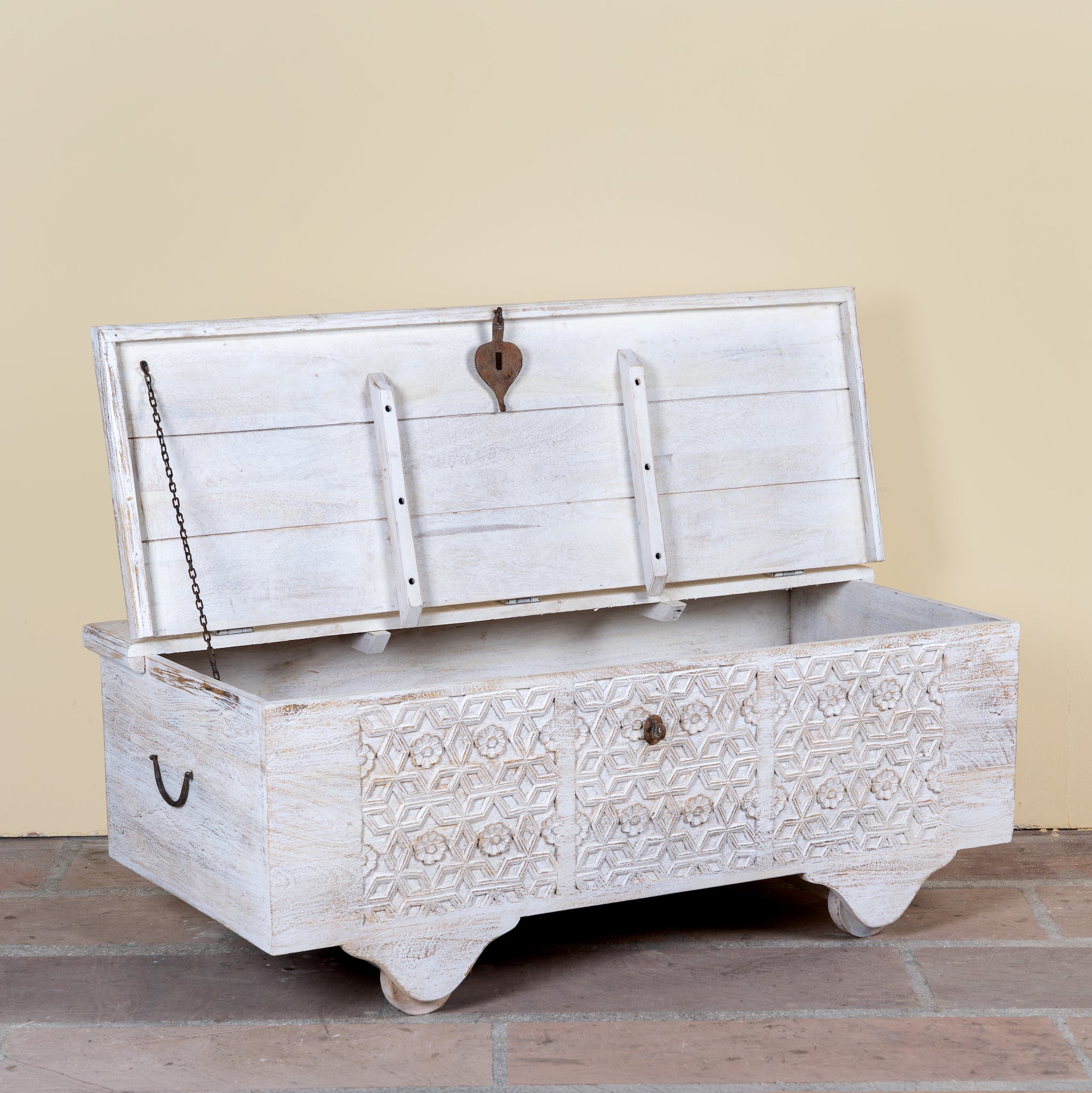 Side angle image showing open lid of a Samay mango wood storage chest coffee table with carved geometric front, iron fittings, wooden wheels and distressed finish 120cm