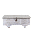 White background image of a Samay mango wood storage chest coffee table with carved geometric front, iron fittings, wooden wheels and distressed finish 120cm