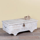 Side angle image of a Samay mango wood storage chest coffee table with carved geometric front, iron fittings, wooden wheels and distressed finish 120cm