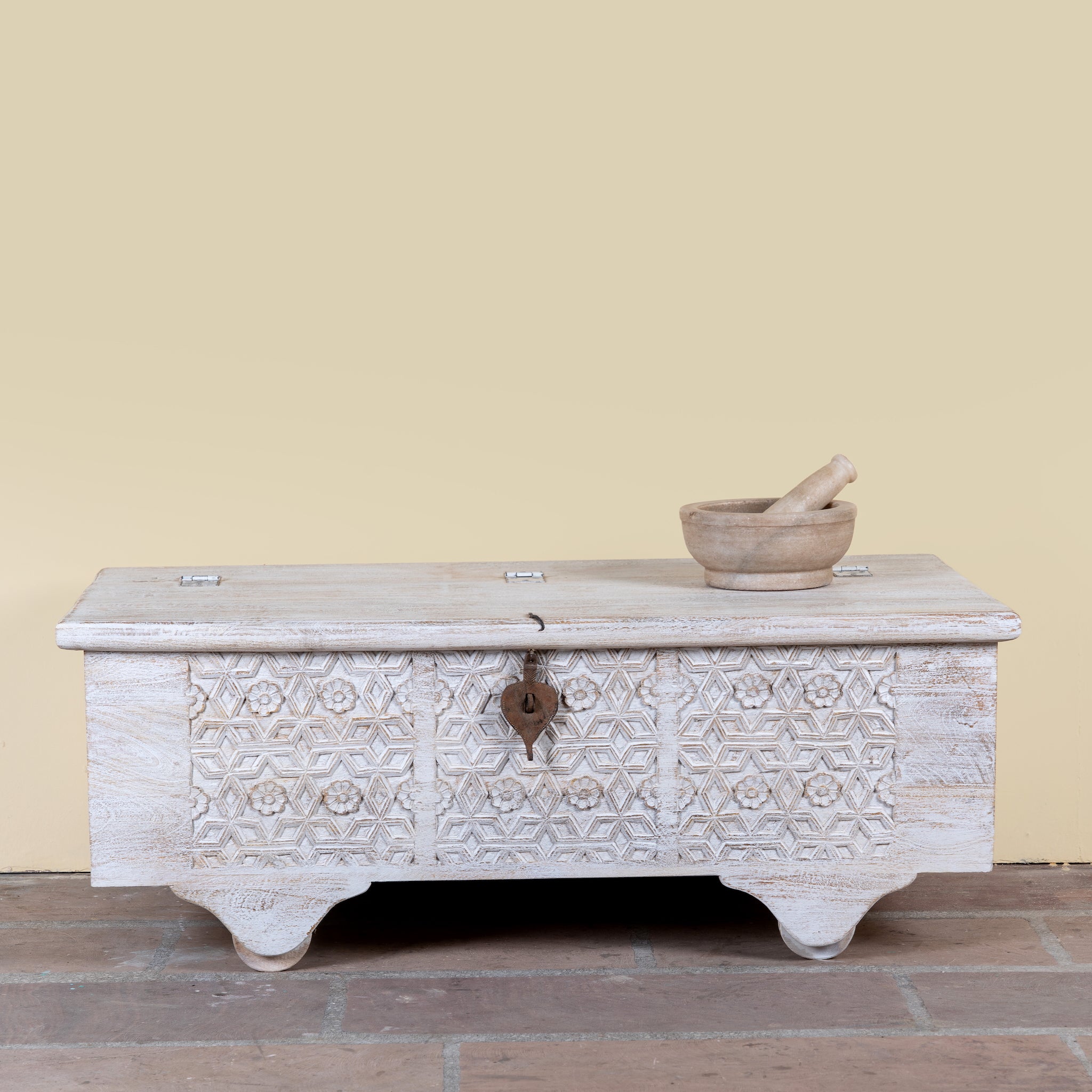 Samay mango wood storage chest coffee table with carved geometric front, iron fittings, wooden wheels and distressed finish 120cm