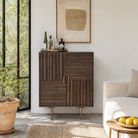 Lifestyle  image of a carved cabinet in mango wood with linear carvings and brass‑plated iron base, 92 × 42 × 115 cm.