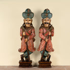 A pair of hand-carved wooden Indian warrior statues with turquoise, red, and black painted details, standing on a beige background.