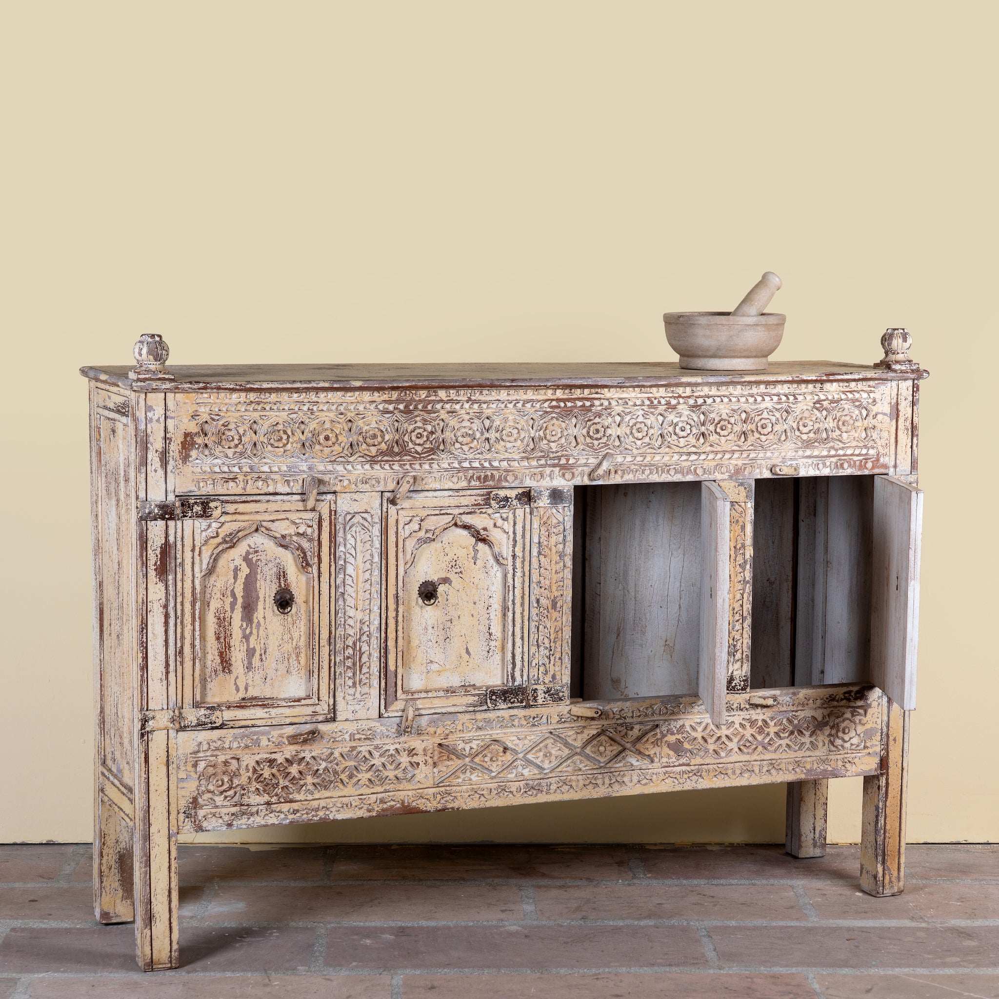 Side angle with open doors image of a Satyam hand carved reclaimed wood sideboard with four arched doors and distressed cream vintage finish 153cm