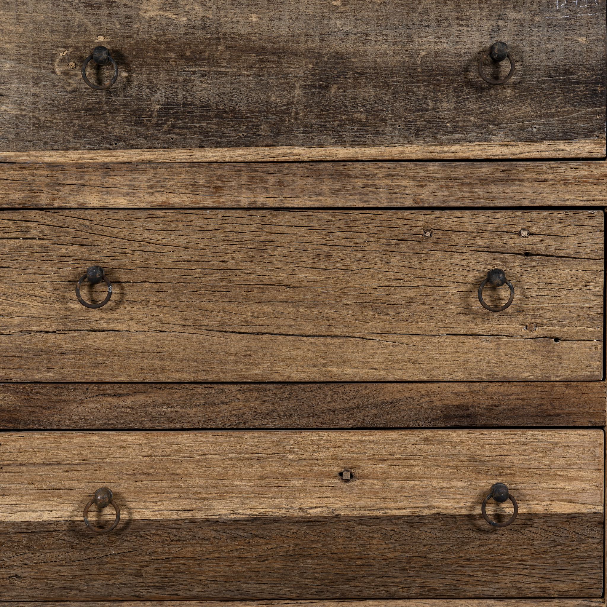 Close up image of a three-drawer dresser in Driftwood/Wabi Sabi style made from recycled old wood, featuring a naturally weathered finish with visible grain patterns and metal ring pull handles for a rustic, handcrafted look.

