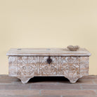 Shaan mango wood storage chest coffee table with carved front, iron fittings, wooden wheels and cream distressed finish 116cm