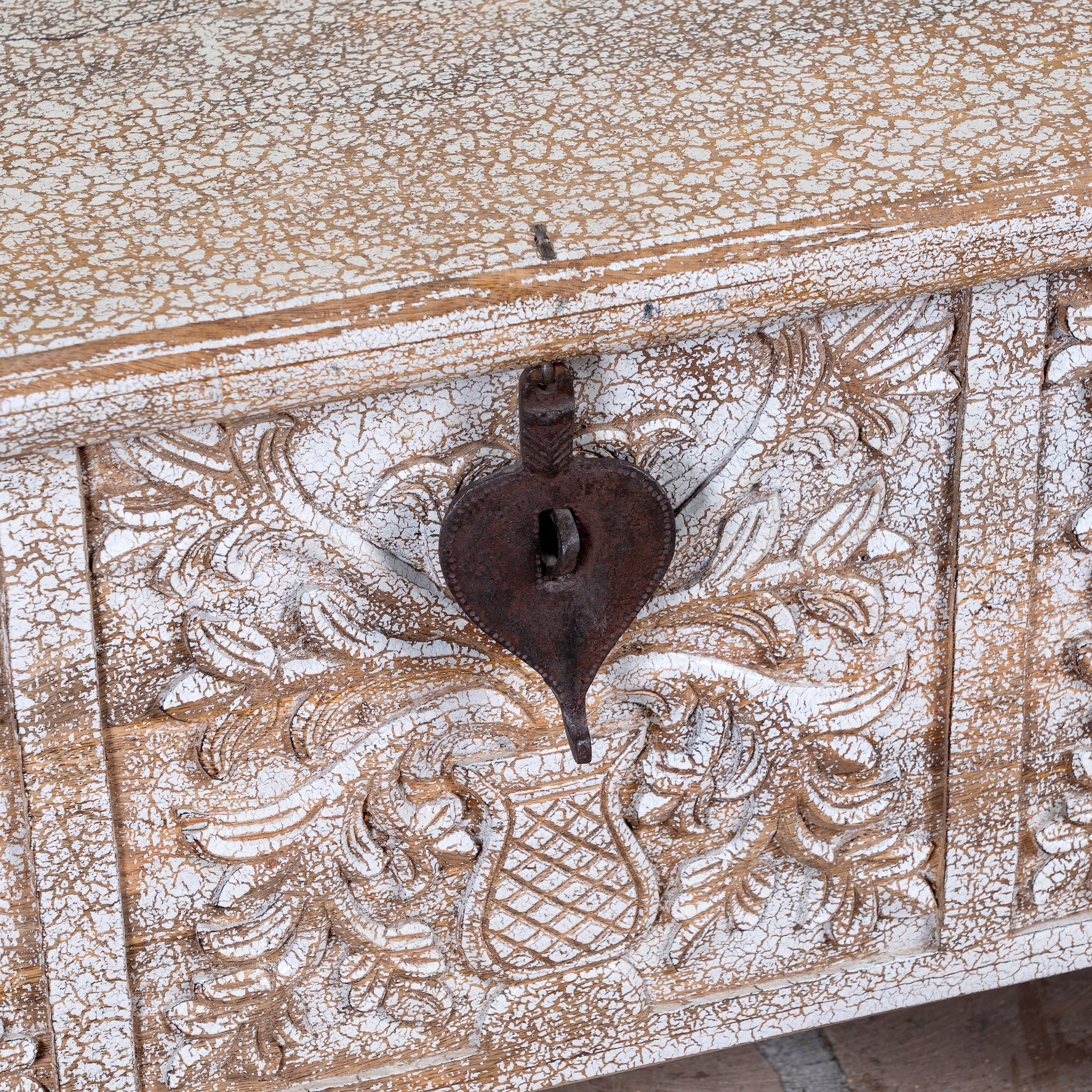 Close up image of a Shaan mango wood storage chest coffee table with carved front, iron fittings, wooden wheels and cream distressed finish 116cm