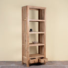 A tall, narrow wooden shelving cabinet with five open shelves and two pull-out drawers at the bottom, shown against a plain beige wall and stone floor.