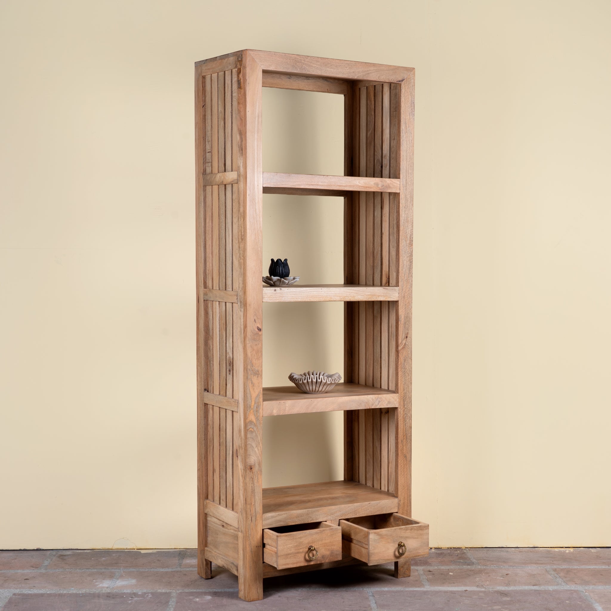 A tall, narrow wooden shelving cabinet with five open shelves and two pull-out drawers at the bottom, shown against a plain beige wall and stone floor.