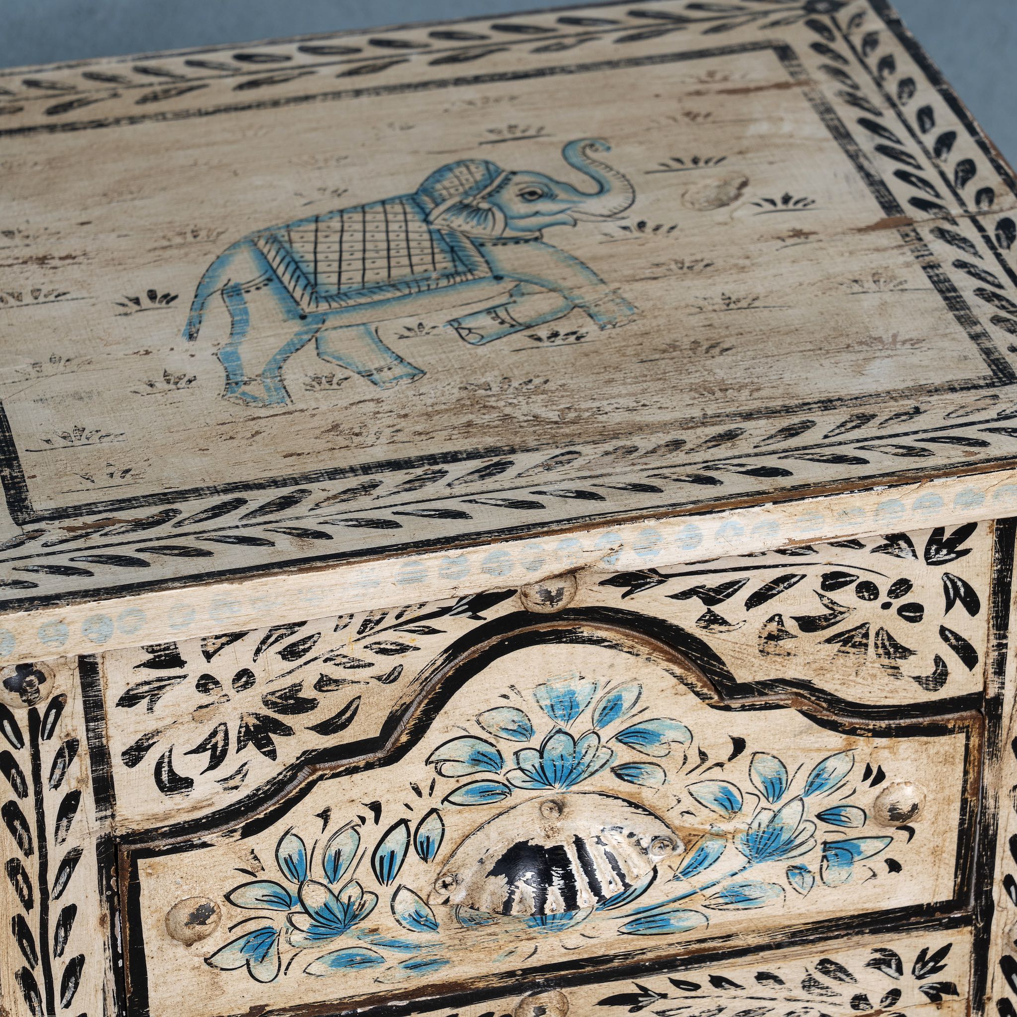 Close up picture of a pair of hand-painted nightstands made from reclaimed wood, featuring floral motifs in soft turquoise and black with intricate carved detailing and two drawers for storage.

