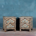 Pair of hand-painted nightstands made from reclaimed wood, featuring floral motifs in soft turquoise and black with intricate carved detailing and two drawers for storage.

