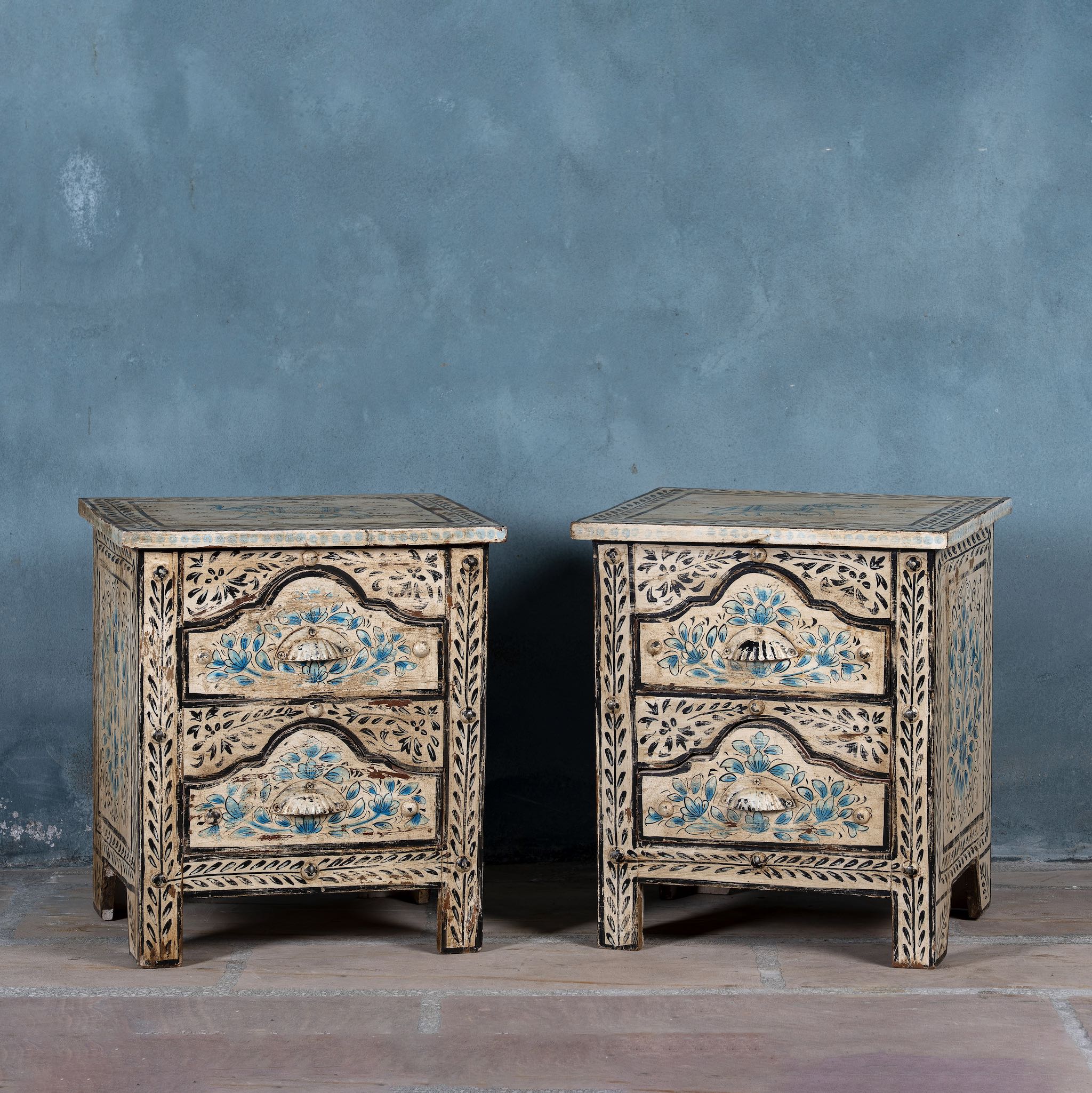 Pair of hand-painted nightstands made from reclaimed wood, featuring floral motifs in soft turquoise and black with intricate carved detailing and two drawers for storage.

