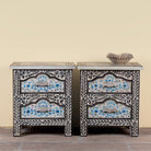 Pair of hand-painted nightstands made from reclaimed wood, featuring floral motifs in soft turquoise and black with intricate carved detailing and two drawers for storage.

