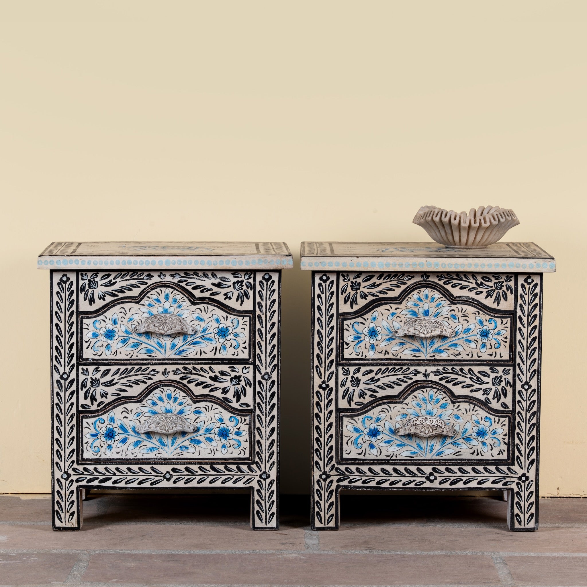 Pair of hand-painted nightstands made from reclaimed wood, featuring floral motifs in soft turquoise and black with intricate carved detailing and two drawers for storage.

