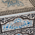 Close up image of a pair of hand-painted nightstands made from reclaimed wood, featuring floral motifs in soft turquoise and black with intricate carved detailing and two drawers for storage.

