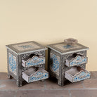 Side angle image with open drawers of a pair of hand-painted nightstands made from reclaimed wood, featuring floral motifs in soft turquoise and black with intricate carved detailing and two drawers for storage.

