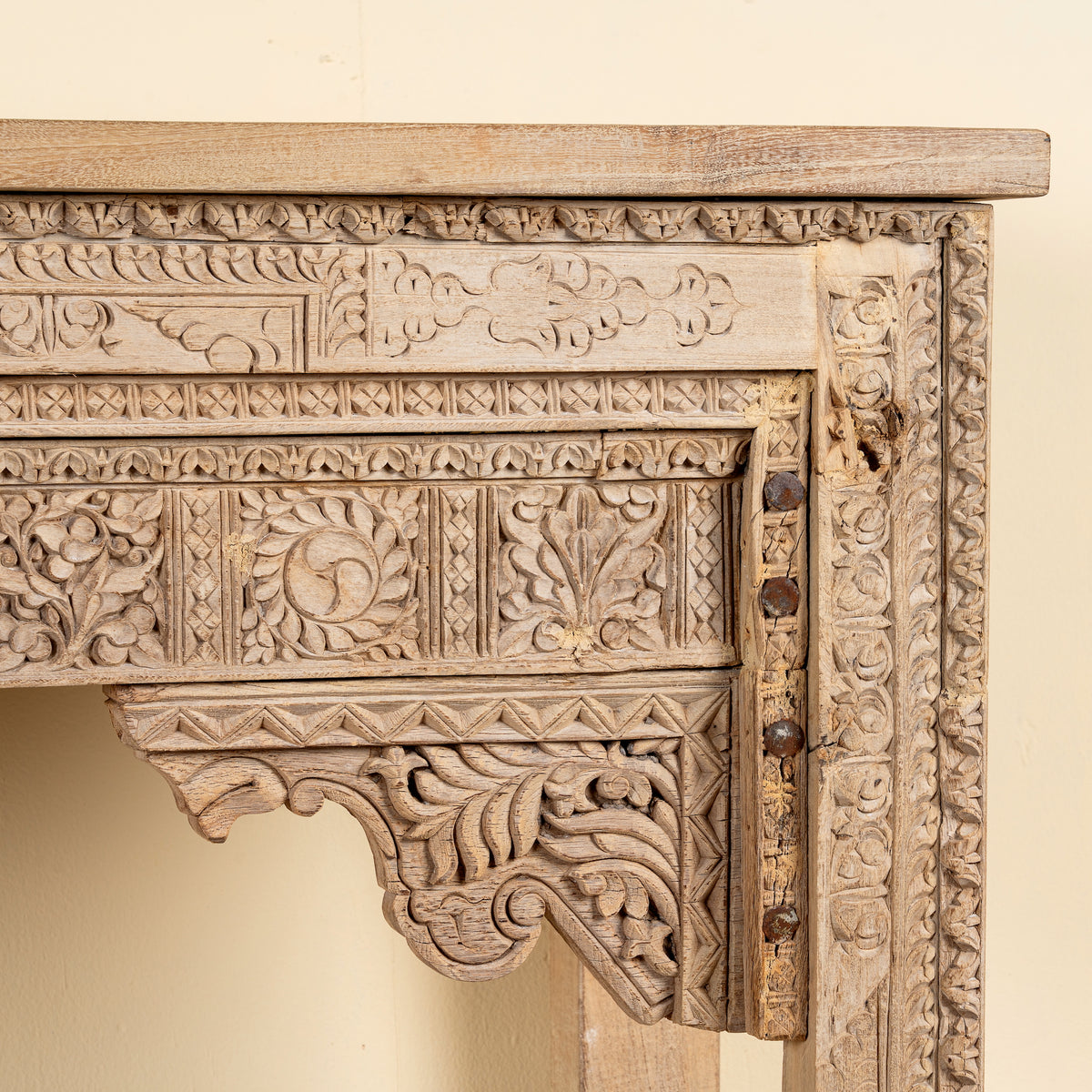 Close up image of a Shivam hand carved reclaimed teak wood console table with decorative old Indian house elements and open storage shelf, 132cm wide.