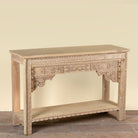 Side angle image of a Shivam hand carved reclaimed teak wood console table with decorative old Indian house elements and open storage shelf, 132cm wide