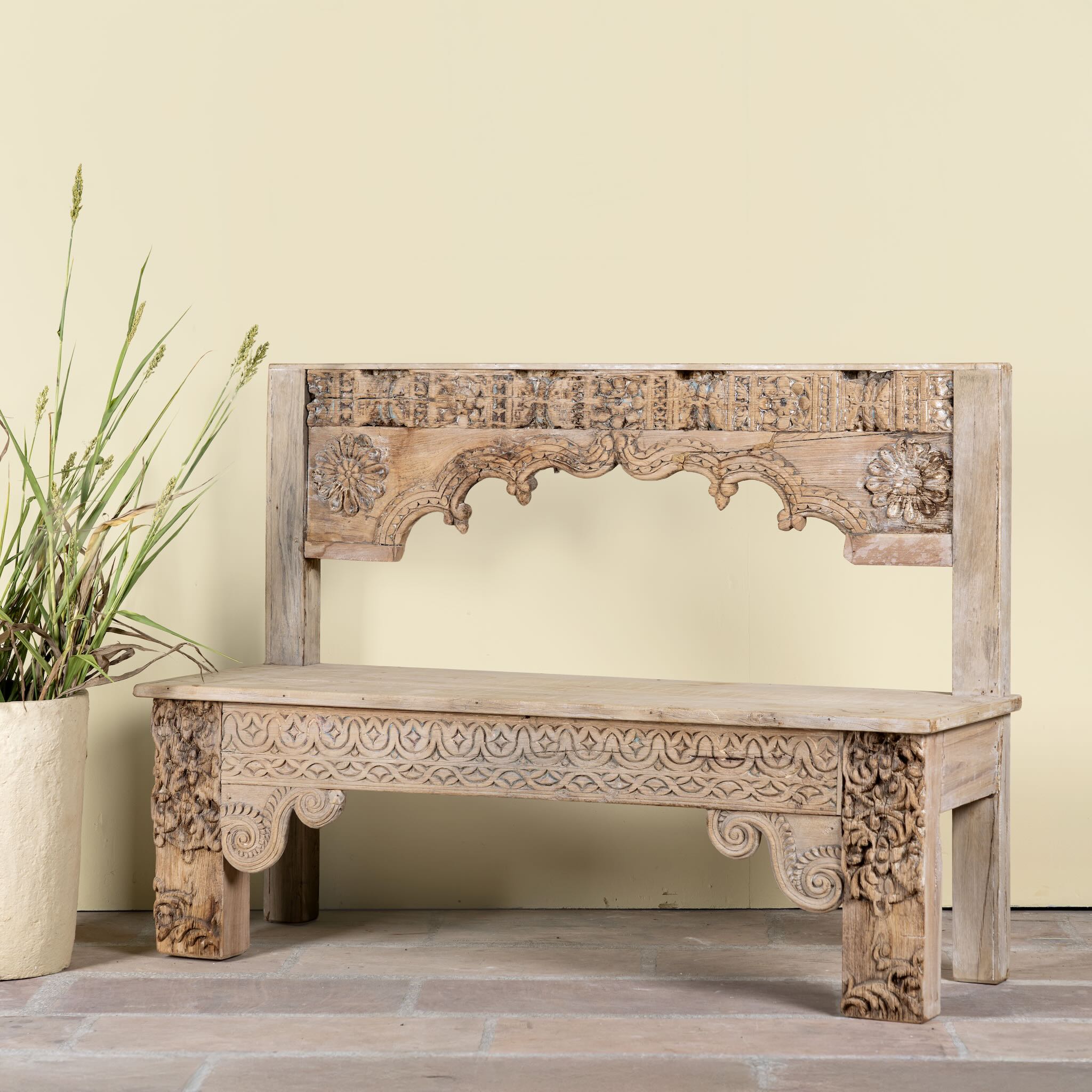 Lifesty;e image of a Shraddha bench made from bleached reclaimed teak wood with intricate hand-carved floral details, showcasing traditional Indian craftsmanship and sustainable furniture design.
