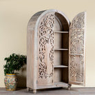 Side angle image with open door of a hand-carved mango wood wardrobe with arched top and intricate peacock floral design – artisanal Indian bedroom furniture.