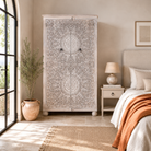 Lifestyle image of a Swara hand carved mango wood wardrobe in bleached Ibiza design with floral mandala doors, hanging rail and shelving, 110x56x190cm