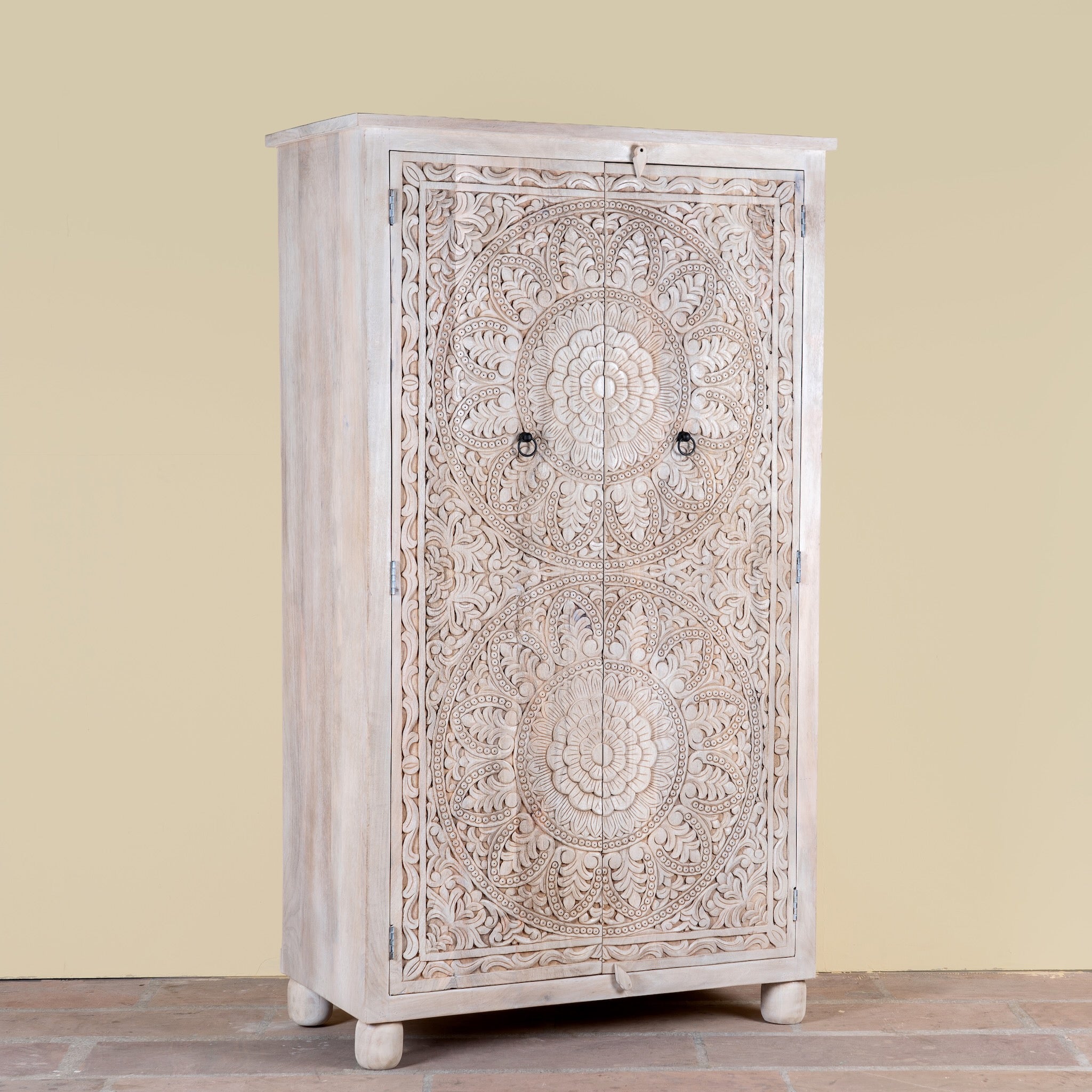 Side angle image of a Swara hand carved mango wood wardrobe in bleached Ibiza design with floral mandala doors, hanging rail and shelving, 110x56x190cm